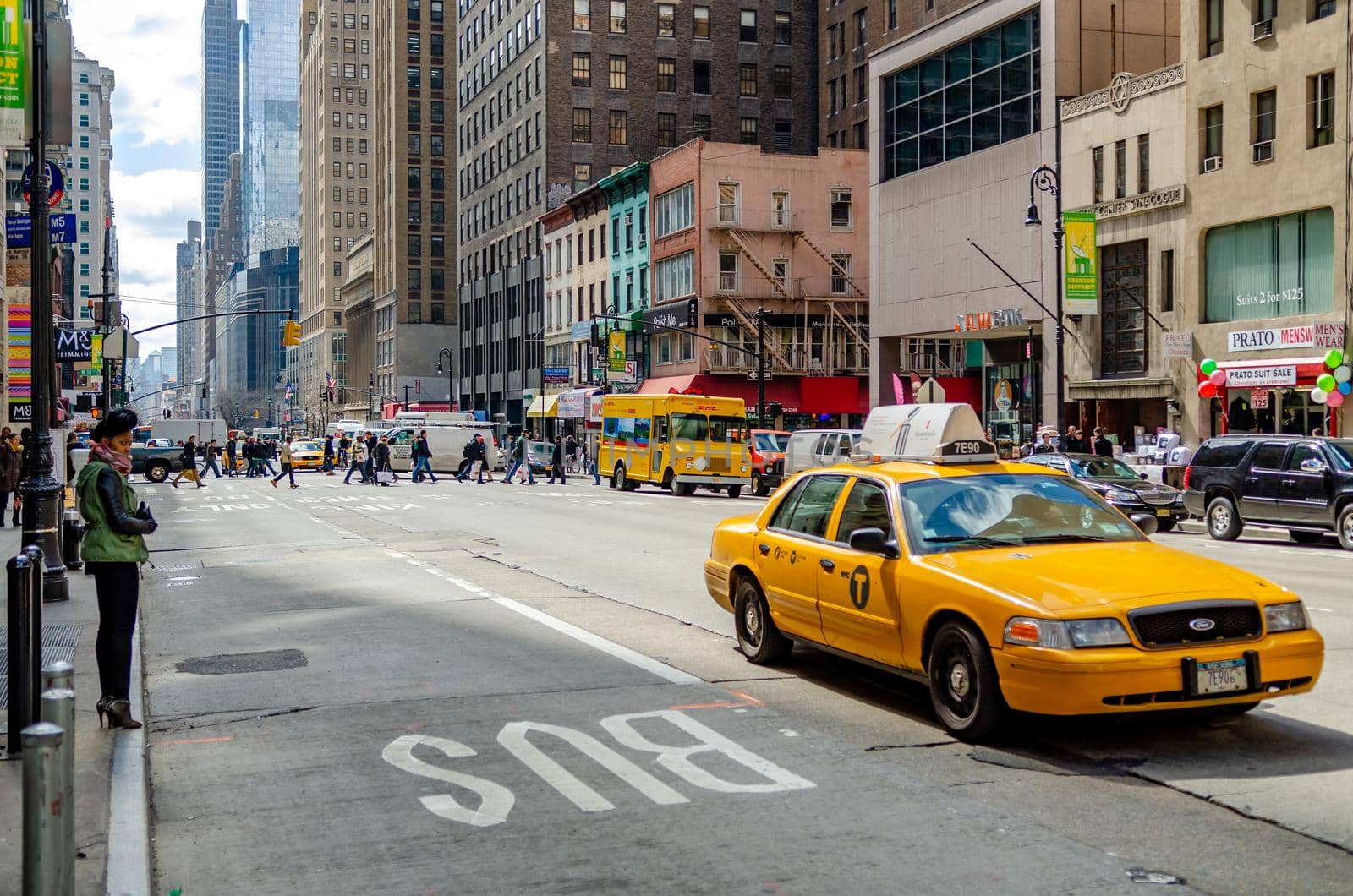 Black Woman standing on the sidewalk of a wide street in Manhattan, New York City, waiting for a Taxi, Only Bus Street in forefront, Lots of traffic and walking People in the background, horizontal