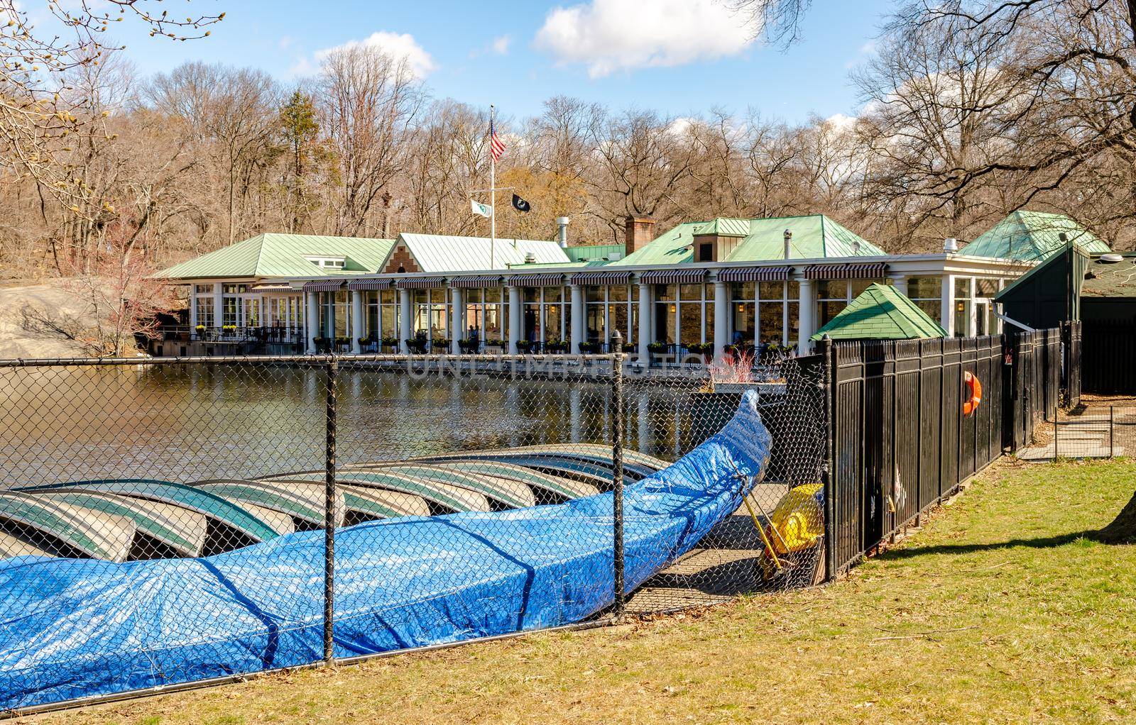 Central Park Boathouse Restaurant, New York City during daylight in winter with fence, boats and lake in the forefront, horizontal