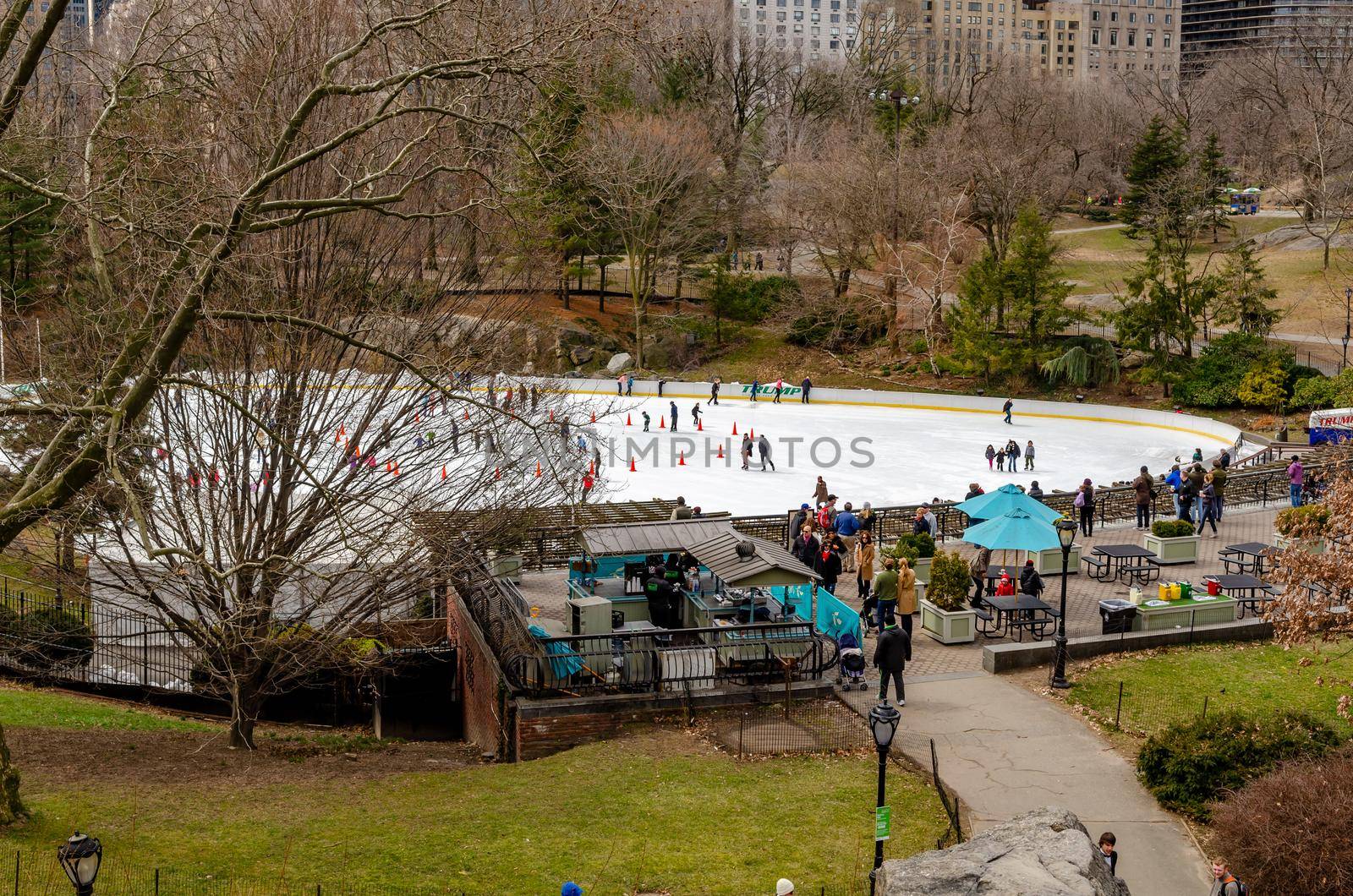 Wollman Rink with People Ice Skating during daytime in winter, view from the distance, Central Park New York City, benches and people walking in the forefront, horizontal