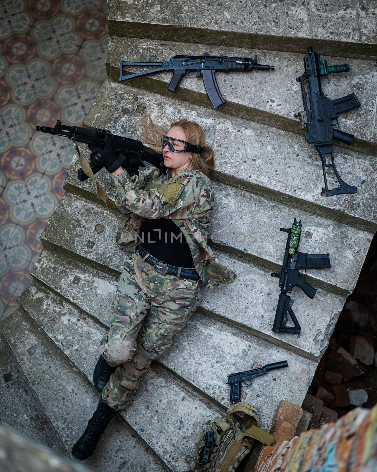Caucasian woman in military uniform lies on the stairs of an abandoned building and holds a machine gun. View from above. by mrwed54