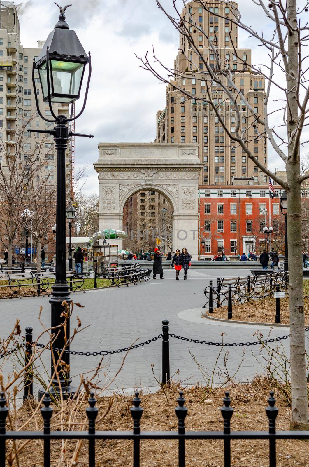 Washington Square Arch, New York City during winter with few People walking in the Park, overcast, street lamp in forefront, view from distance, vertical