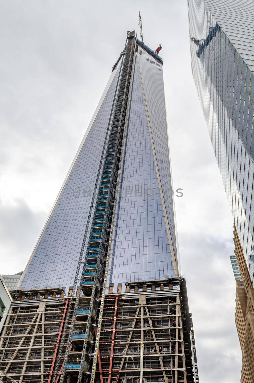 One World Trade Center construction area with crane on top during daytime with overcast, New York City, view from low angle, vertical