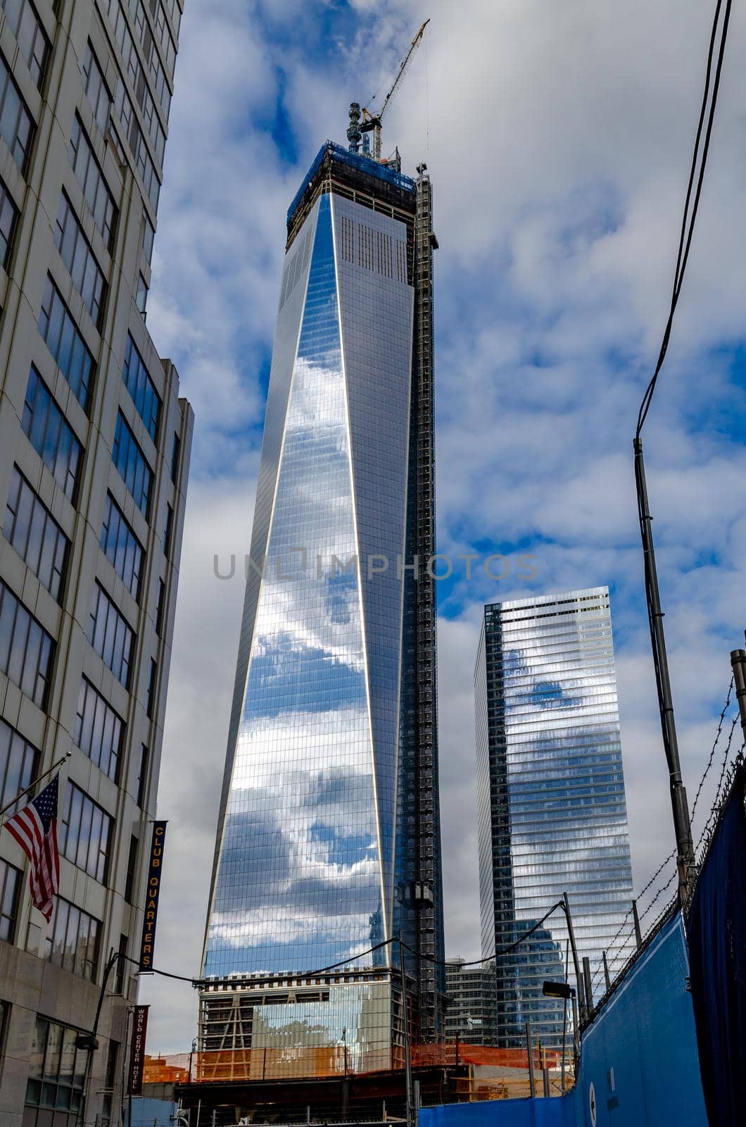 One World Trade Center construction area with  clouds reflection in the window, crane on top during daytime with overcast, New York City, view from low angle, vertical