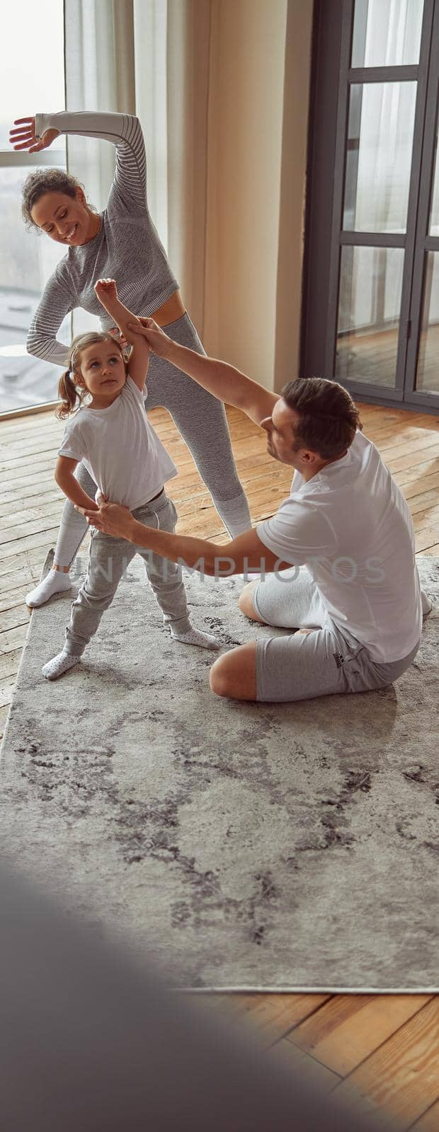 Jolly sporty family doing gymnastics together indoors by Yaroslav_astakhov