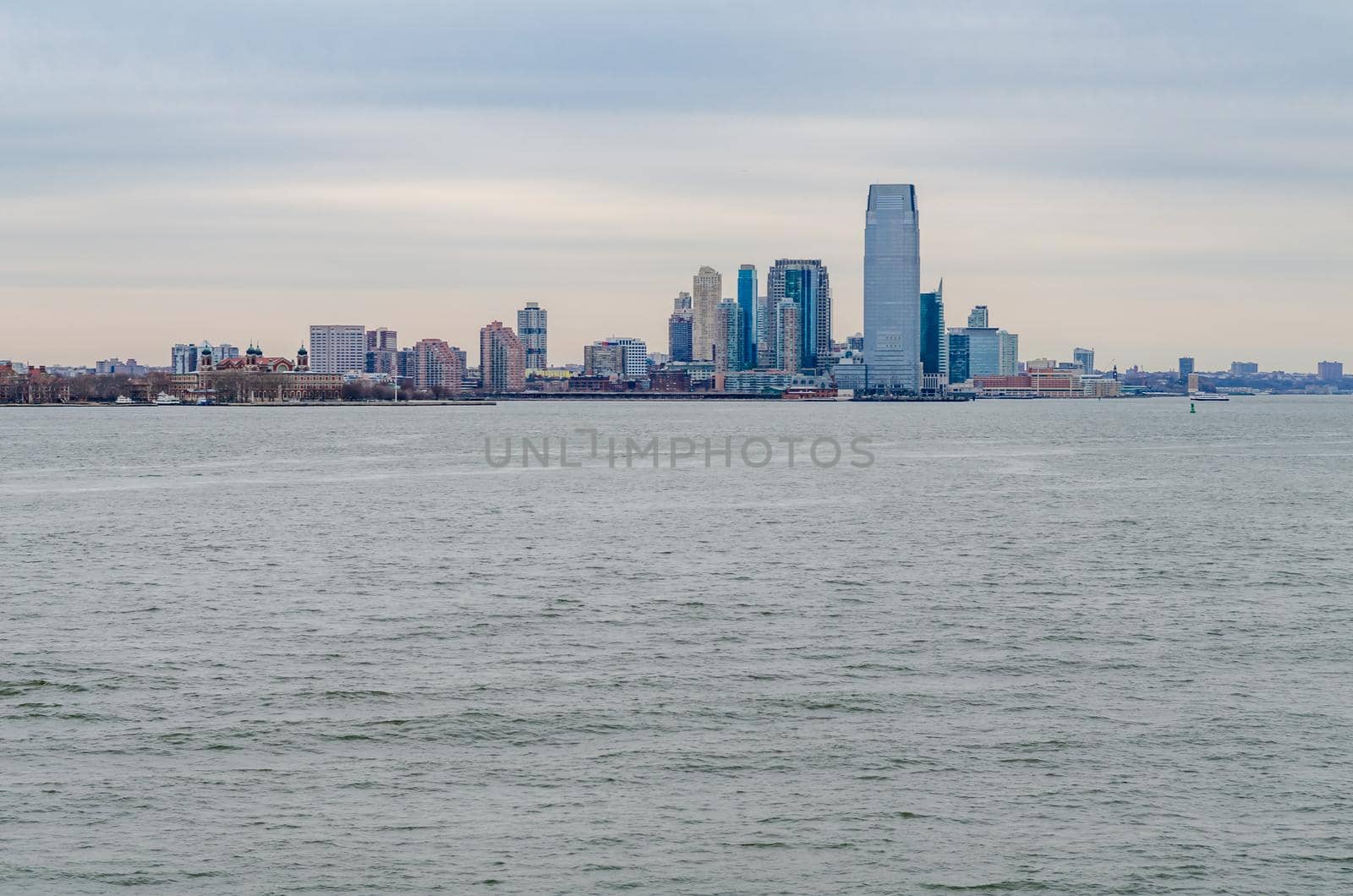 Jersey City, New Jersey with office building skyscraper, Hudson river in forefront, during winter evening with overcast, horizontal