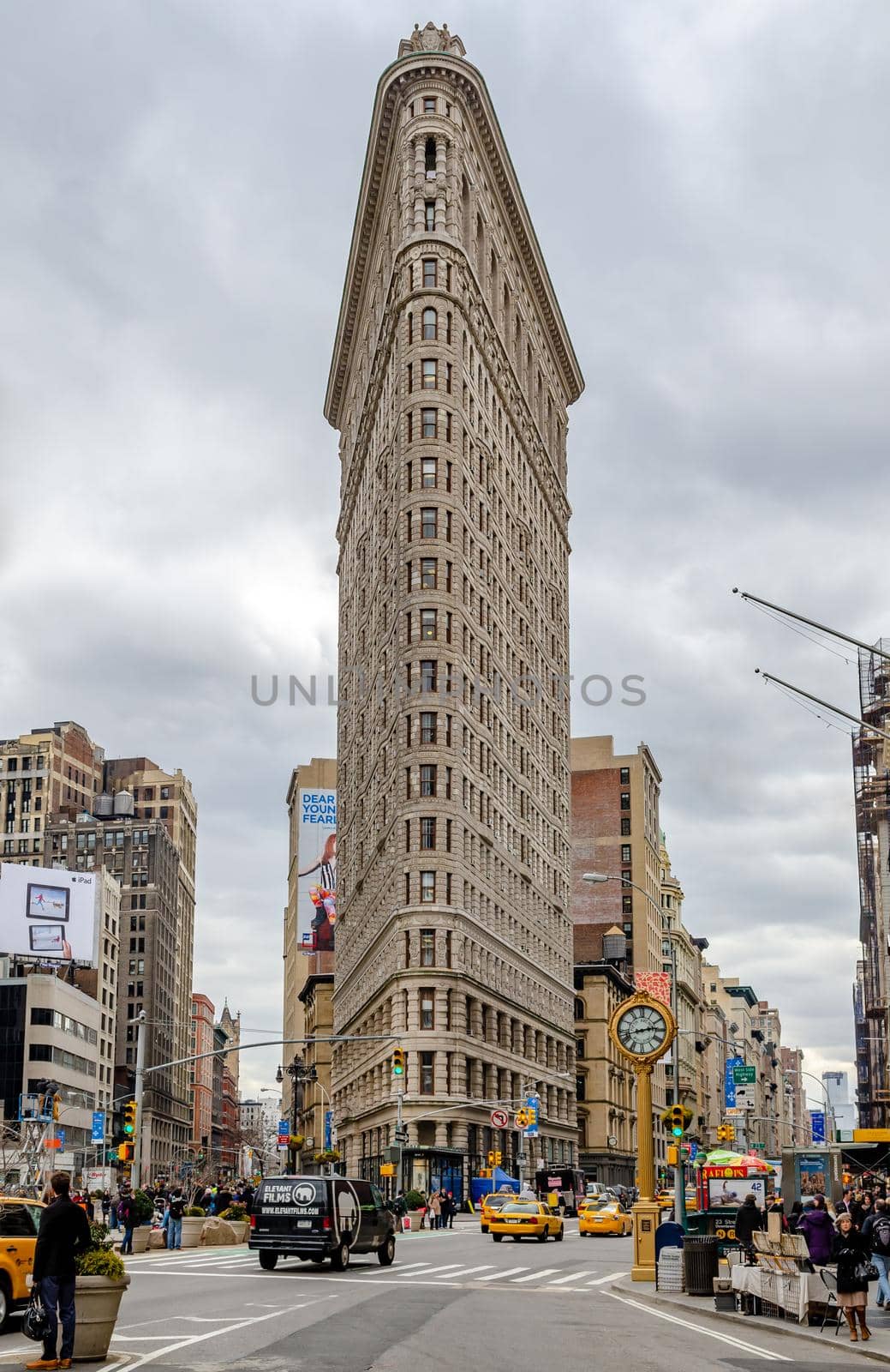 Flatiron Building New York City with street and crosswalks, yellow taxi cabs in forefront during daytime with overcast, view from low angle, vertical