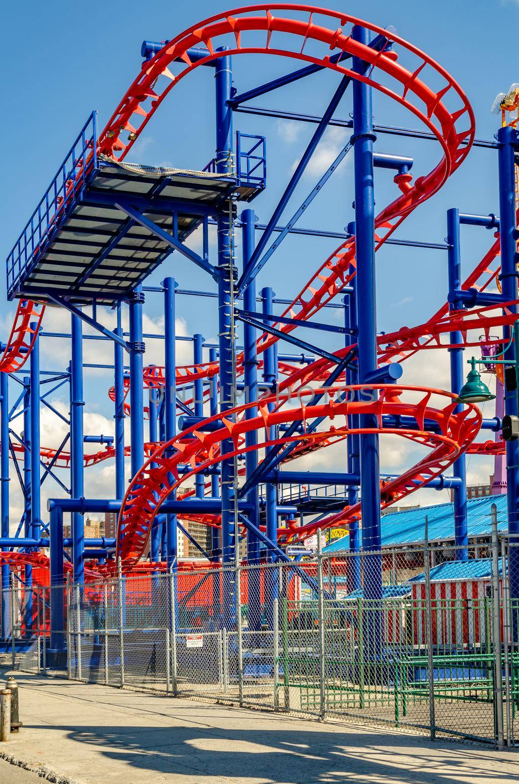 Soarin' Eagle Rollercoaster red and blue colored, close-up at Luna Park Amusement Park, Coney island, Brooklyn, New York City during winter day with clear sky, view from low angle with fence in front, vertical