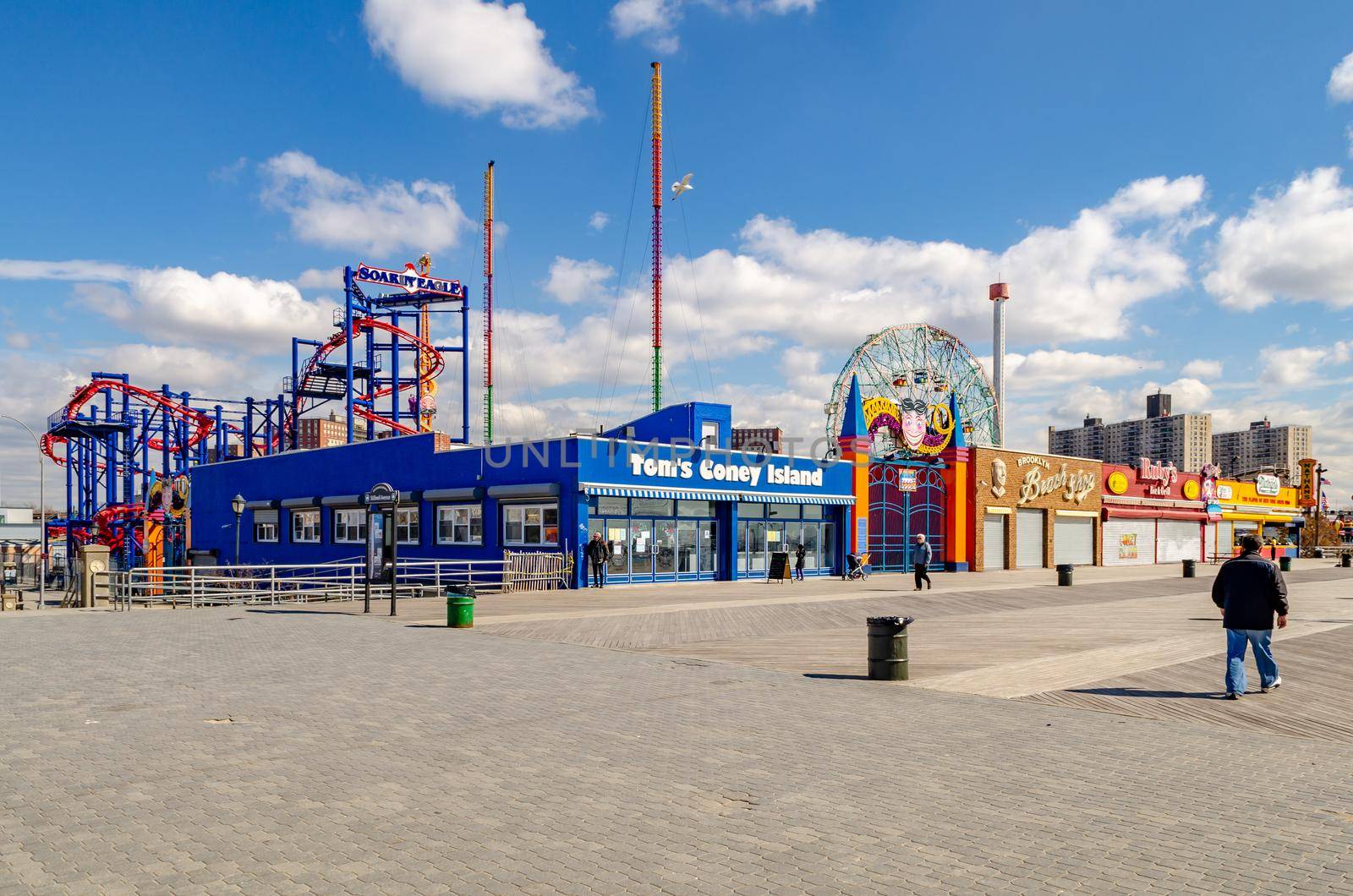 Tom's Coney island, Brooklyn Restaurant with Soarin' Eagle Rollercoaster, Wonder Wheel and Beach Promenade at Luna Park Amusement Park, Coney island, Brooklyn, New York City during winter day with clear sky, People walking at the Promenade, horizontal