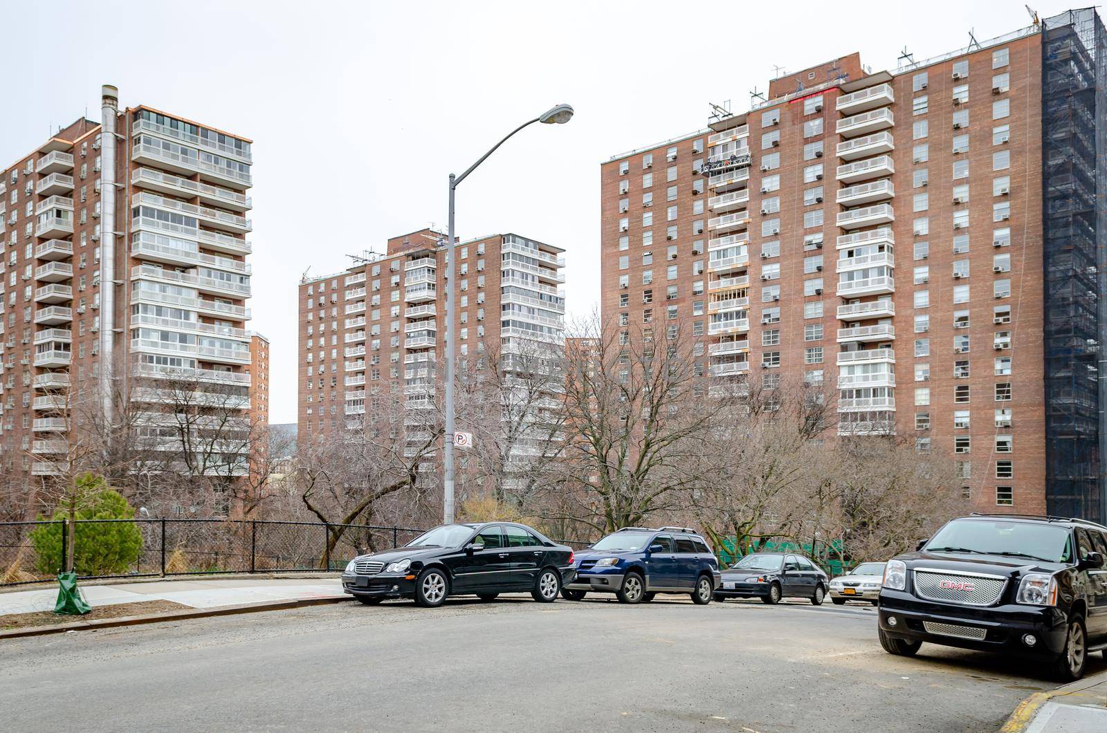Residential Area with old brown apartment skyscrapers in Harlem, New York City, during winter day with overcast, Cars parked in the forefront on the street, horizontal