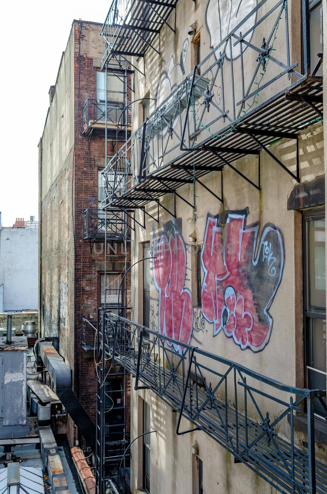 Rustic Residential Building Facade in Chelsea with Graffiti on the Wall, Emergency stairs at the Building, New York City during sunny winter day, vertical