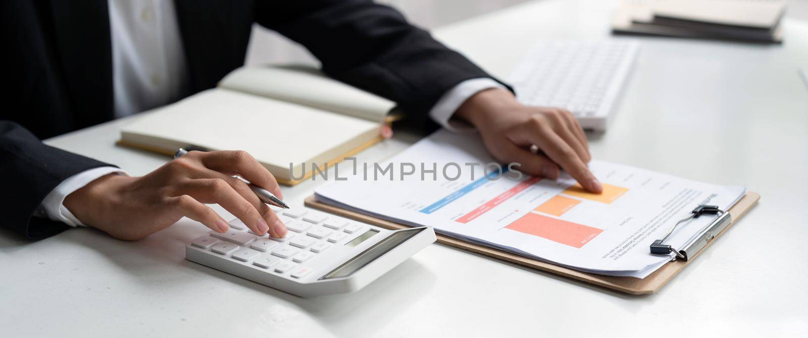 Close up of businessman or accountant hand holding pen working on calculator to calculate business data, accountancy document and laptop computer at office, business concept.