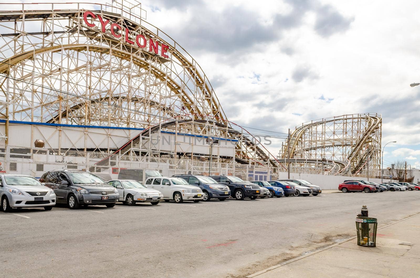 Cyclone Wooden Rollercoaster at Luna Park Amusement Park, Coney island, Brooklyn, view from the side with lots of cars parked in front next to the street, New York City during winter day with cloudy sky, horizontal
