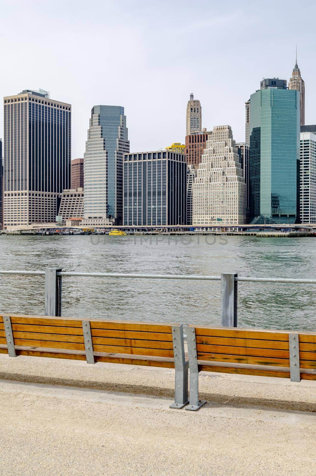 Skyline of Manhattan, New York City, view from waterfront in Brooklyn, wood benches standing in front of a fence at the river bank, vertical