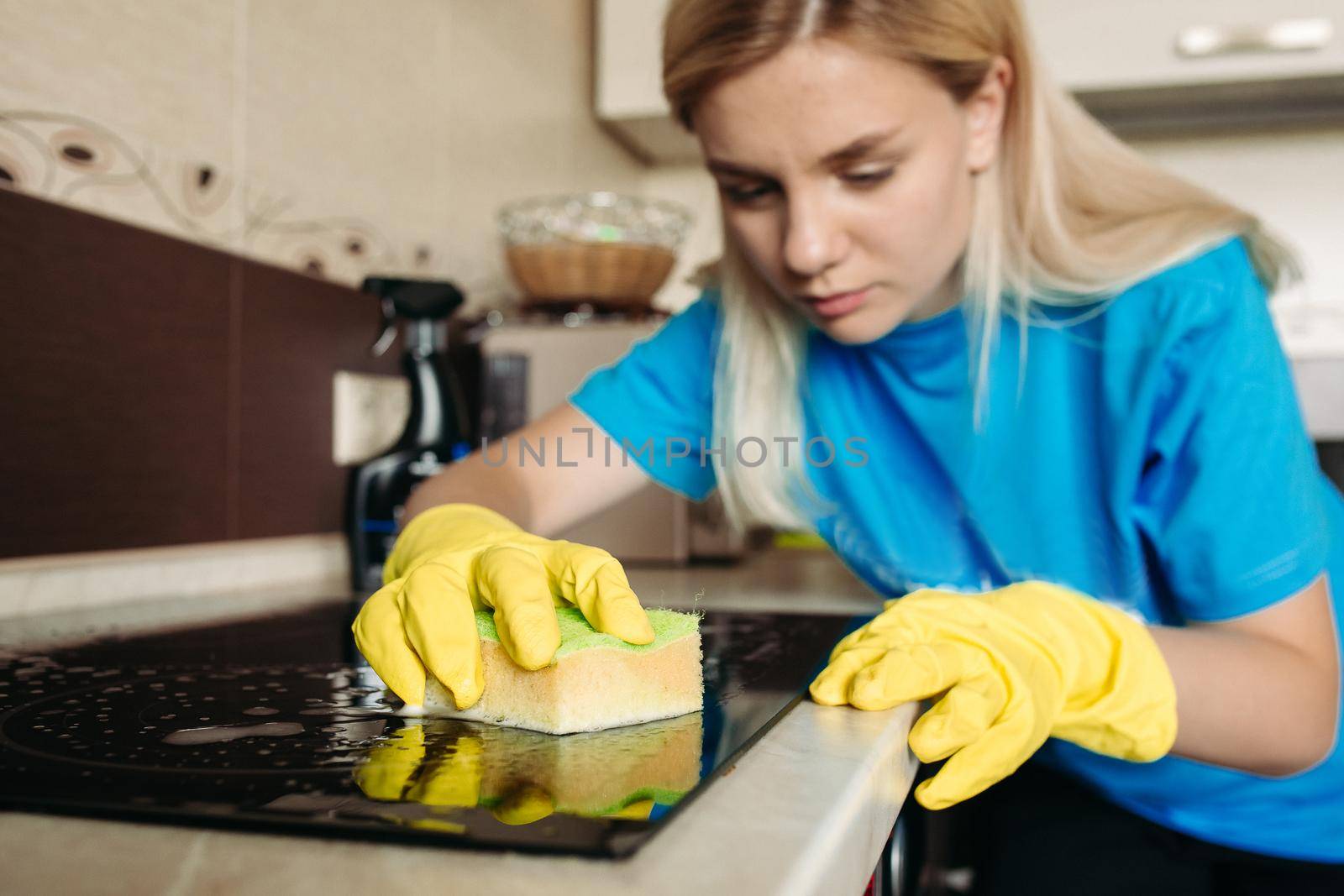 Close up of woman, wearing in protective glove with rag cleaning electric stove at home kitchen. Beautiful girl washing black shiny surface of kitchen top, hand with foam on sponge. Housework concept.