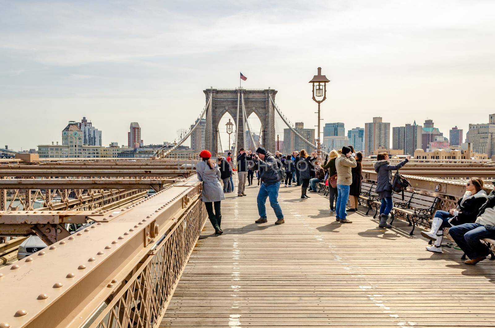 Brooklyn Bridge New York City in the evening during winter with tourists walking, taking photos and relaxing on benches on the bridge, wide angle shot, skyscraper in the background, horizontal