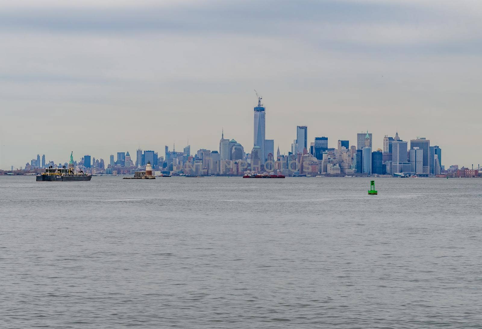 Skyline of Manhattan, New York City with Hudson river in forefront during winter day with overcast, wide angle shot from the distance, view from Staten island, during winter day with overcast, ships and lighthouse in the forefront, horizontal