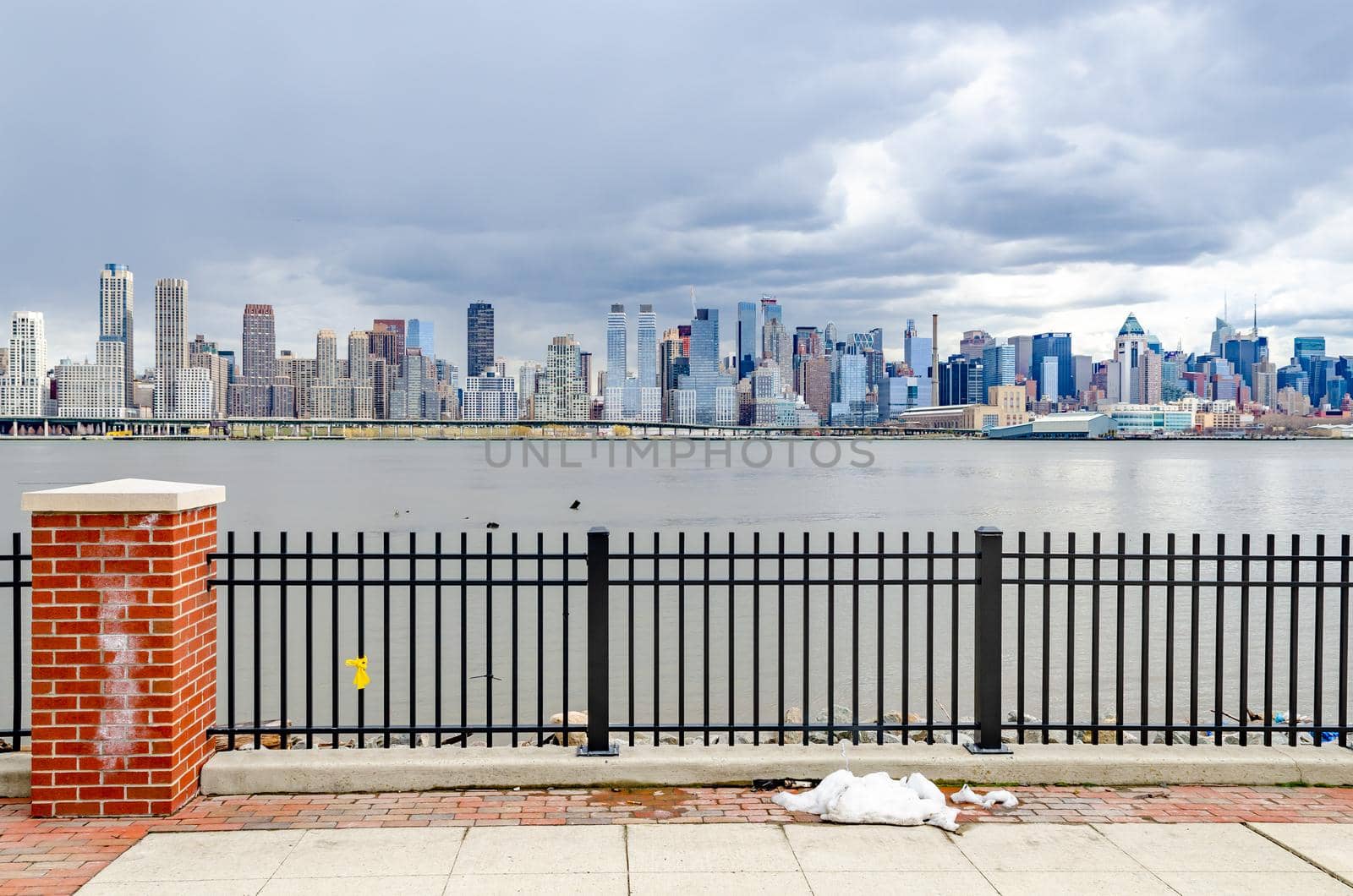View of Manhattan from the Other side of Hudson River with fence in front, New Jersey during cloudy winter day, snow on the ground, horizontal