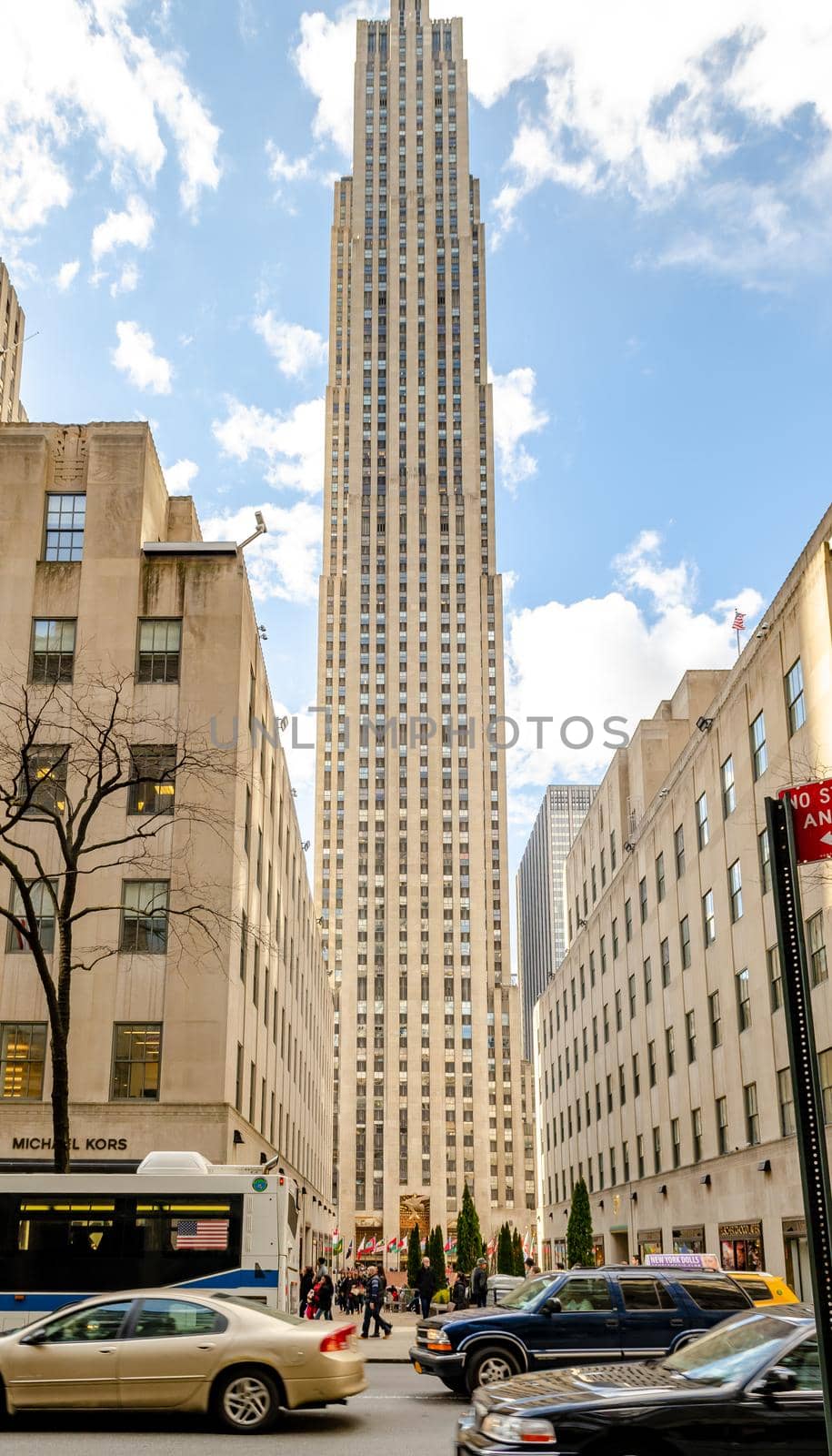 Rockefeller Center with City street and Cars, Bus and Taxi passing by in front during sunny winter day with cloudy sky, vertical