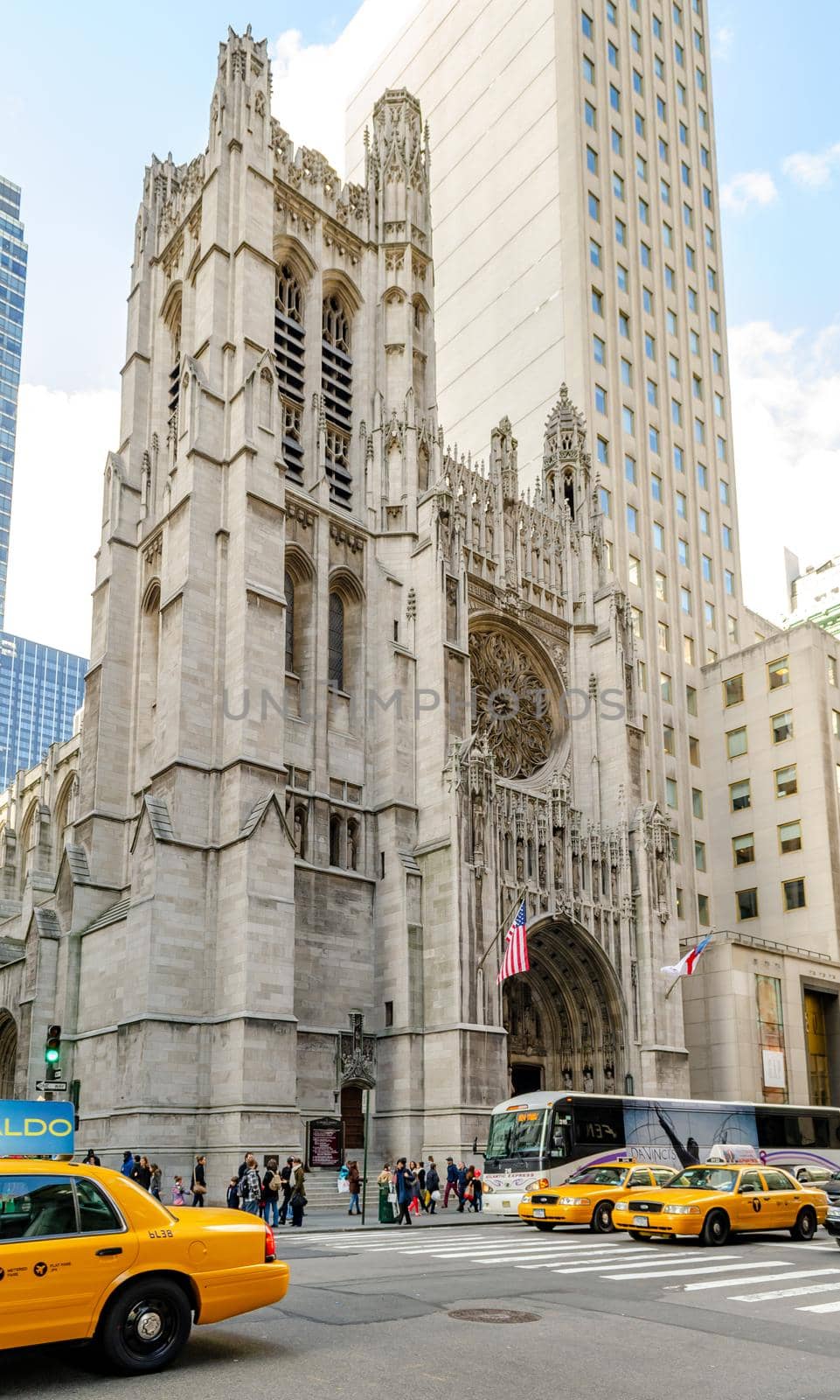 Saint Thomas Church with yellow taxis and a bus in front waiting at crosswalk, view from low angle, Manhattan, New York City during sunny winter day with cloudy sky, vertical