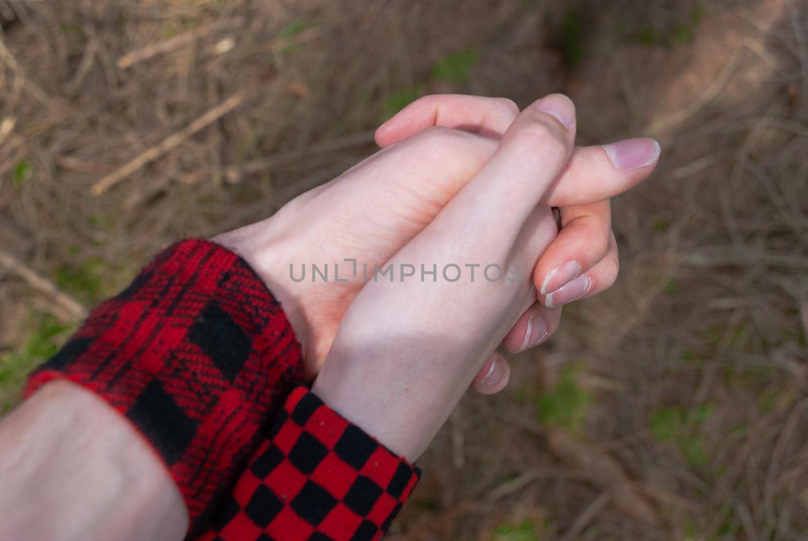 Punk emo couple holding hands, wearing red checkered armbinde while walking outdoors in the forest, close-up