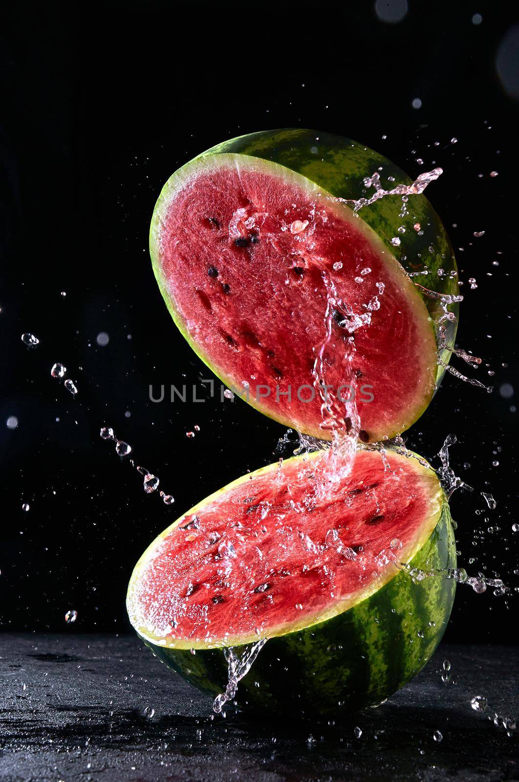 Ripe watermelon cut in half with water splash flying in the air.