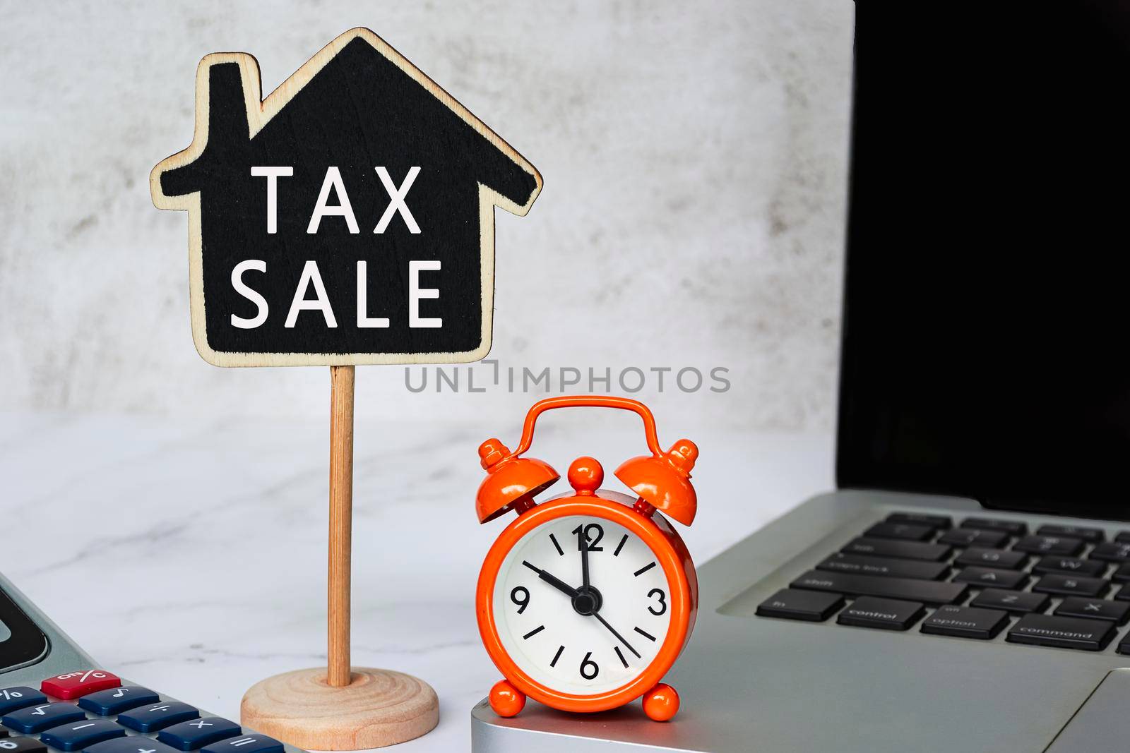 Tax Sale text on wooden house model with notebook and calculator on white table. Real estate property tax concept.