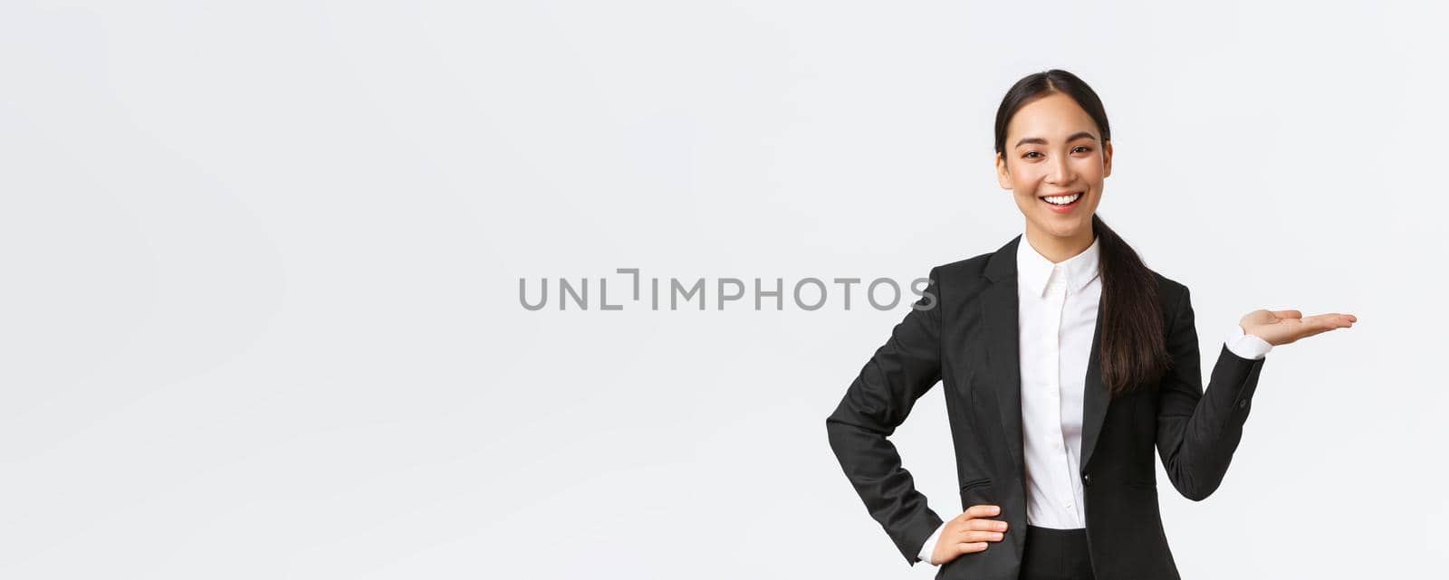 Professional smiling businesswoman introduce her project during meeting. Saleswoman in black suit holding hand right as showing product, holding on palm over blank white background.