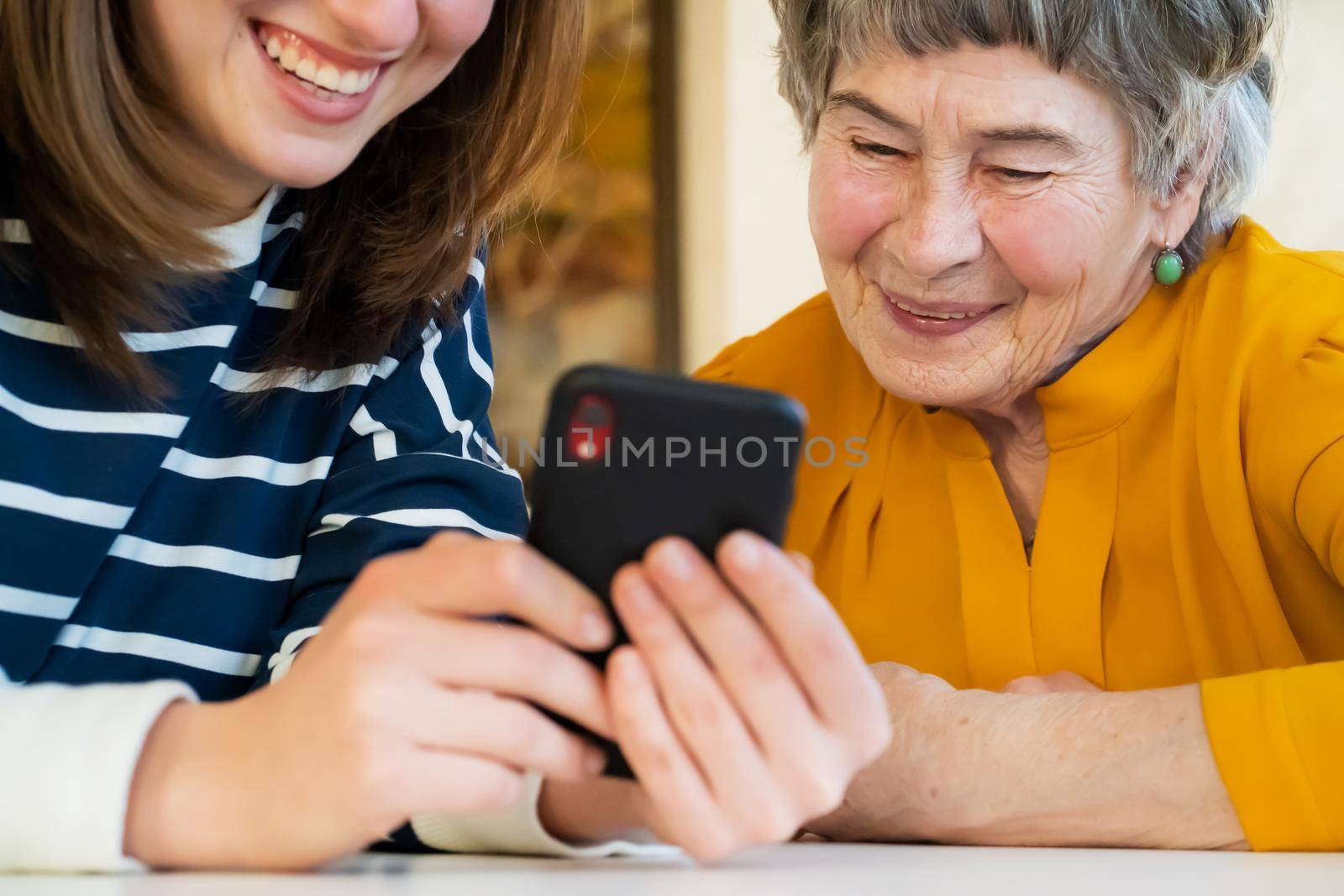 Young girl, a granddaughter, explains to an elderly relative how to use a smartphone and an application to communicate with a doctor at home. The family loves and cares for their elderly parents.