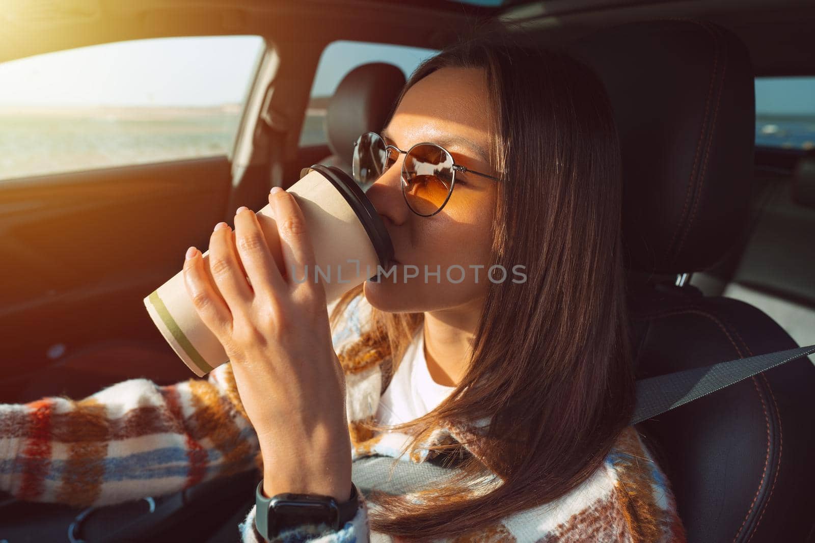 Young beautiful woman driving a car and drinking coffee. by DariaKulkova
