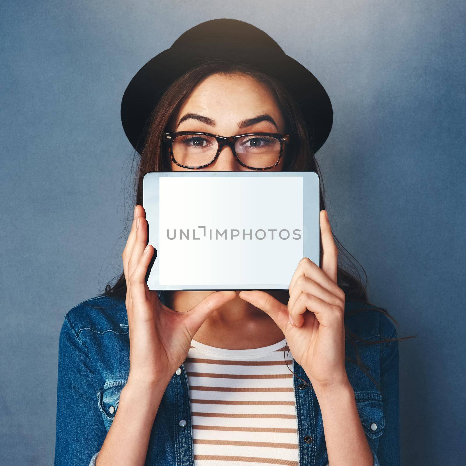 Have I got the app for you. Shot of an attractive young woman holding tablet in front of her face in studio. by YuriArcurs
