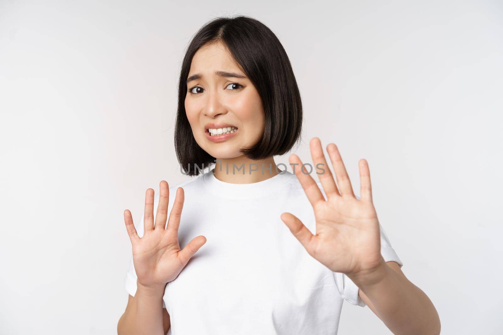 Disgusted asian woman rejecting smth, grimacing from dislike and aversion, stare with cringe, refusing offer, standing over white background.