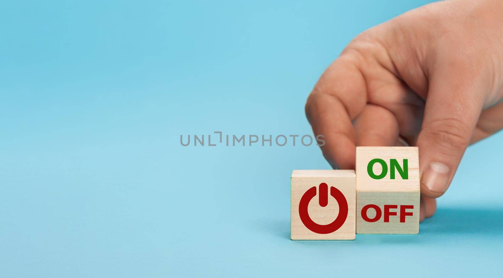 Hand turns a dice and changes the word off to on. Switch button on a wooden cube with inscriptions on and off word on a blue background. Start-stop button