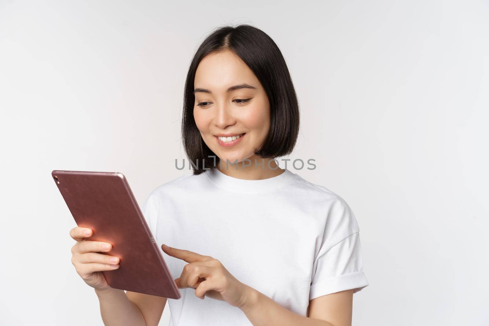 Asian girl using digital tablet, working with gadget, shopping online, standing over white background.