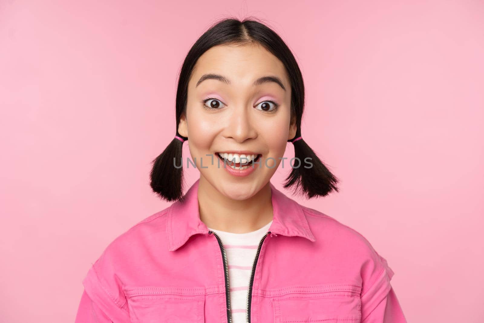 Close up portrait of beautiful asian girl looking enthusiastic and smiling, laughing and smiling, standing happy against pink background.