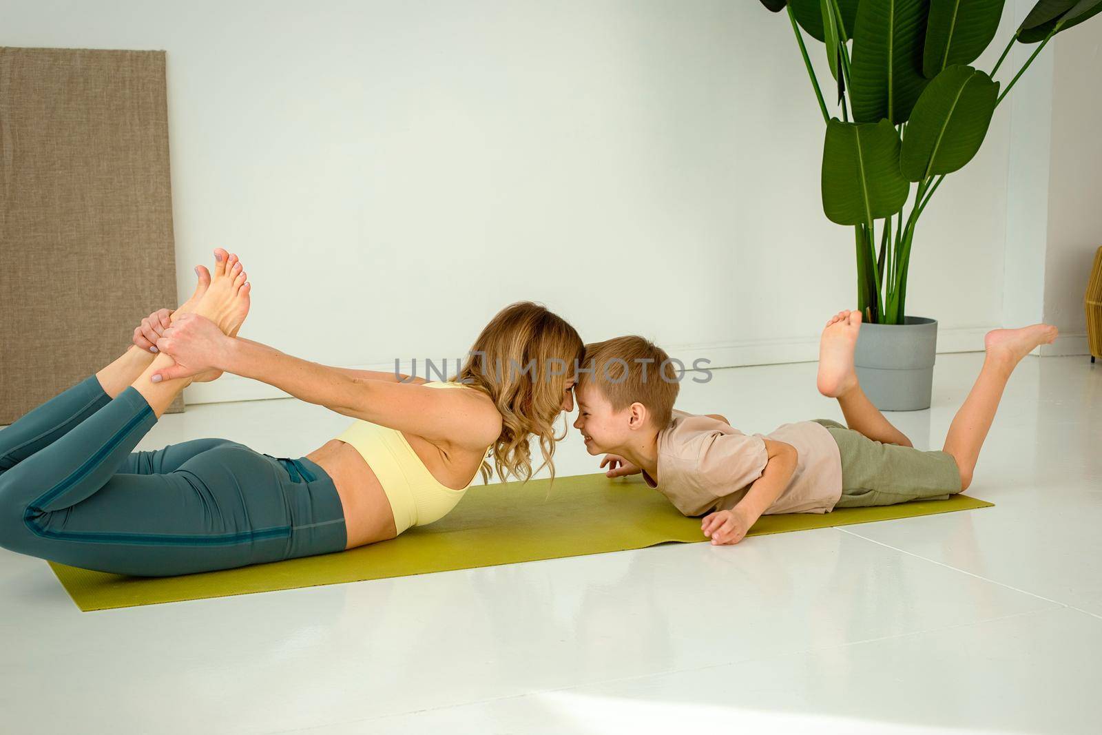 Happy woman doing yoga with a little cute boy lies on a green gym mat in the room. copy space.