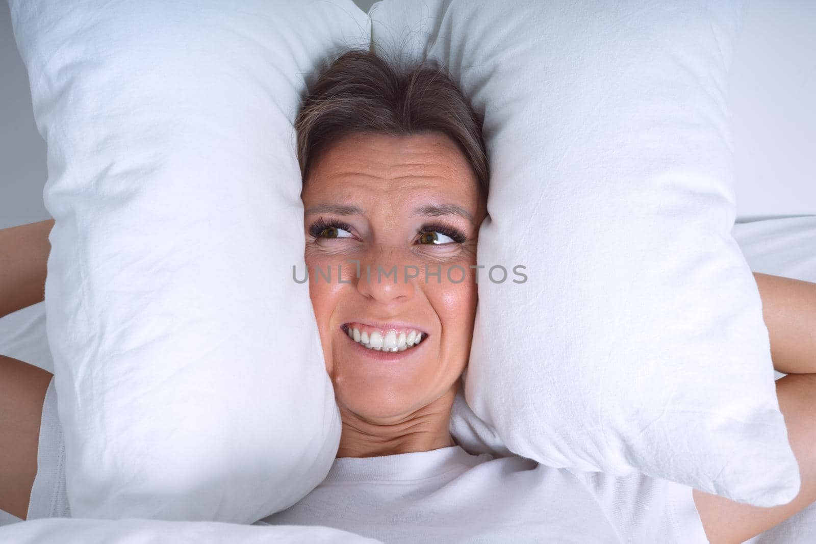 Young woman disturbed by noisy neighbours. Woman struggling from noise in bed and covering ears with pillows. High quality photo