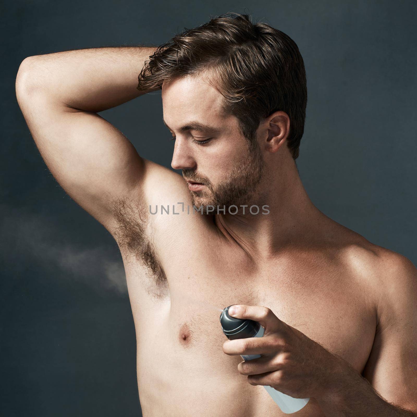 Cropped shot of a handsome young man spraying deodorant on his armpit.