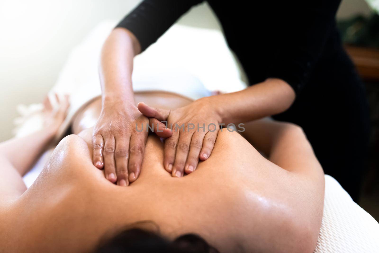 Female therapist giving back massage to young woman. Close up hands. Bodycare concept.