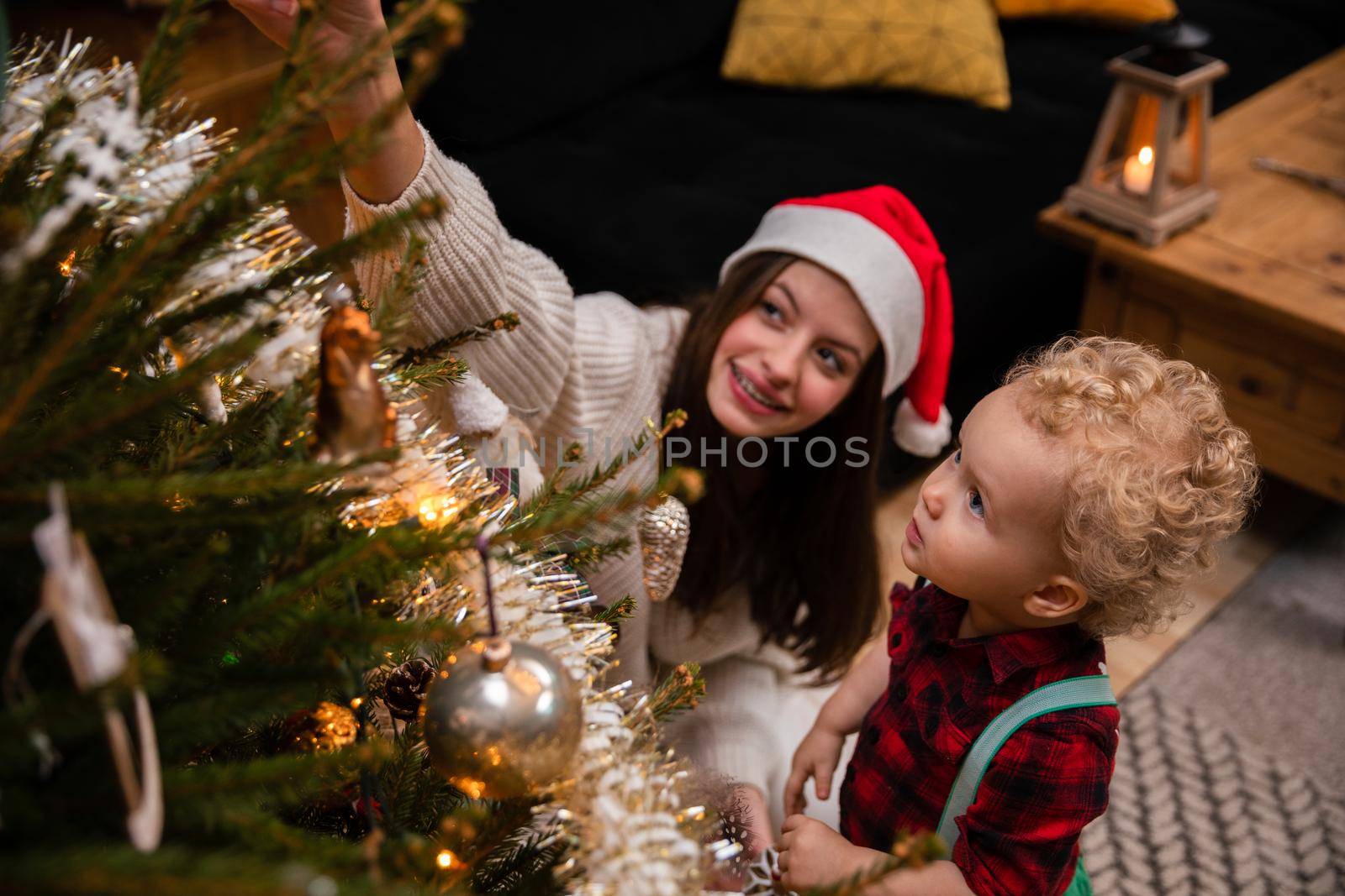 A caring sister tells her brother about Christmas tree decorations. A two-year-old child with curly blonde hair and a teenage brunette as brother and sister.