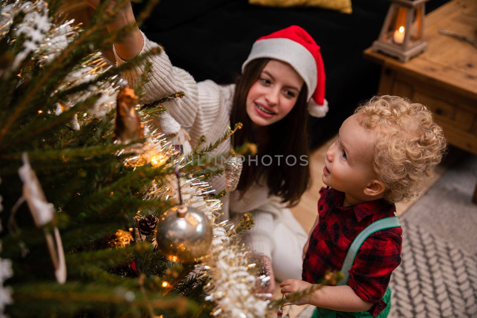 A caring sister tells her brother about Christmas tree decorations. A two-year-old child with curly blonde hair and a teenage brunette as brother and sister.