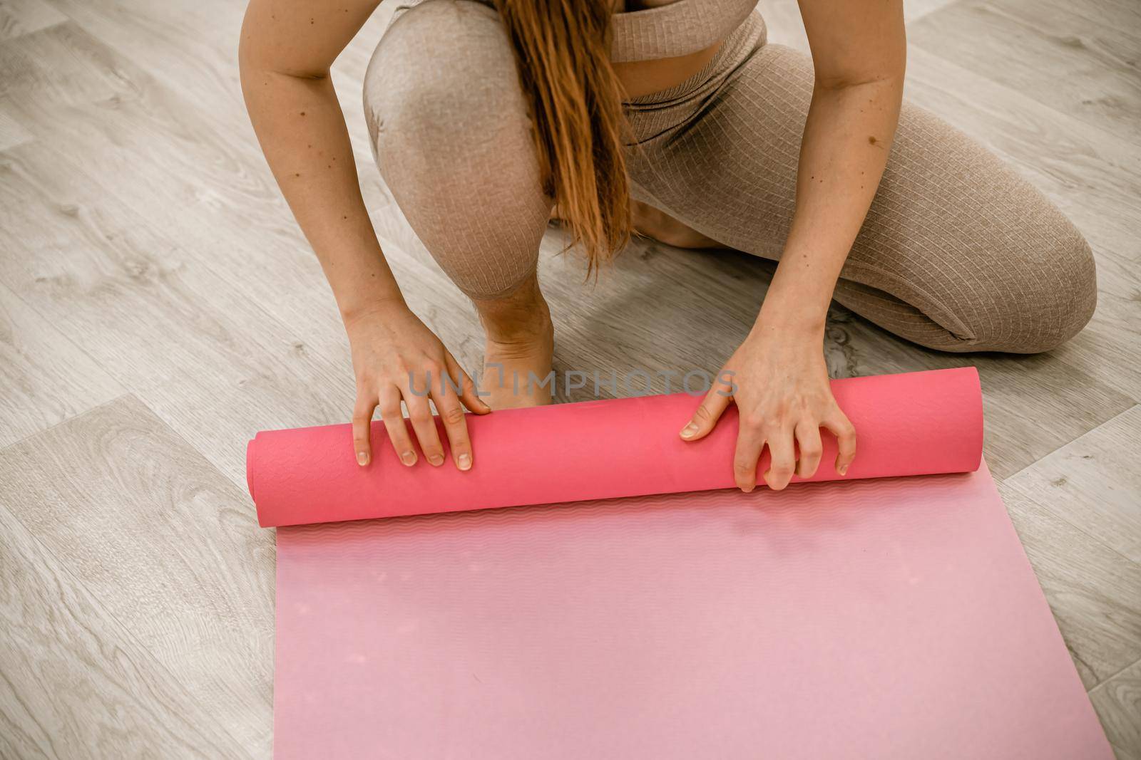 A young woman rolls a pink fitness or yoga mat before or after exercising, exercising at home in the living room or in a yoga studio. Healthy habits, keep fit, weight loss concept. Closeup photo.