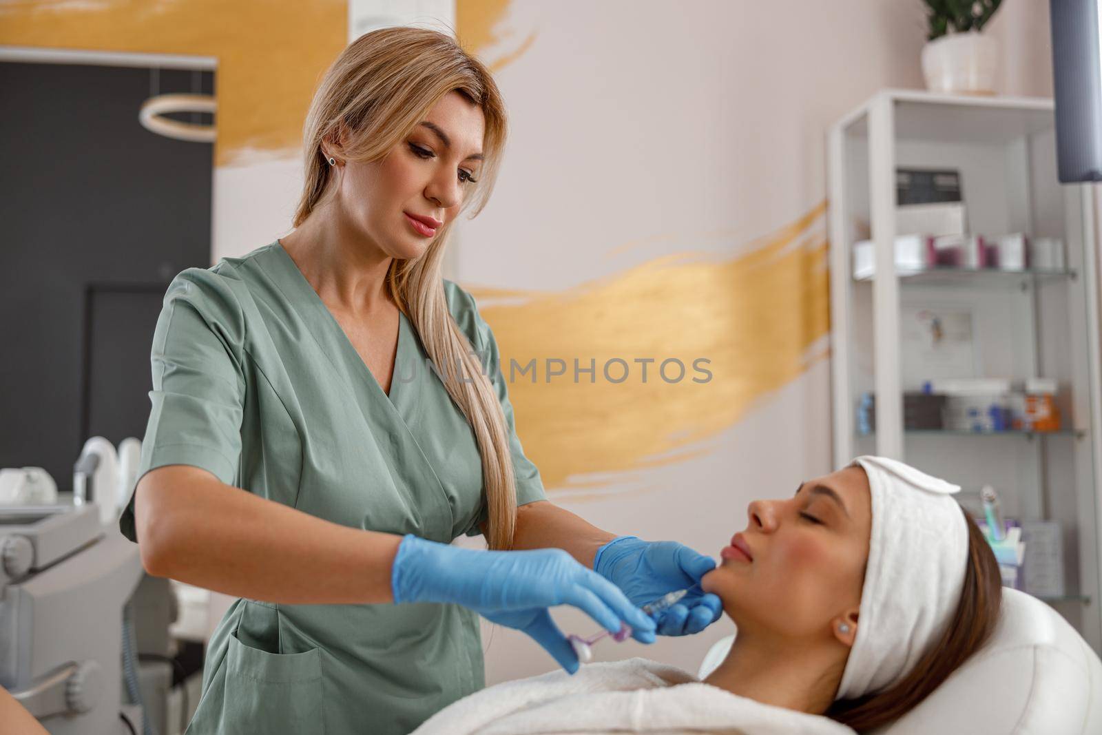 Expert beautician filling female chin with hyaluronic acid in beauty salon by Yaroslav_astakhov