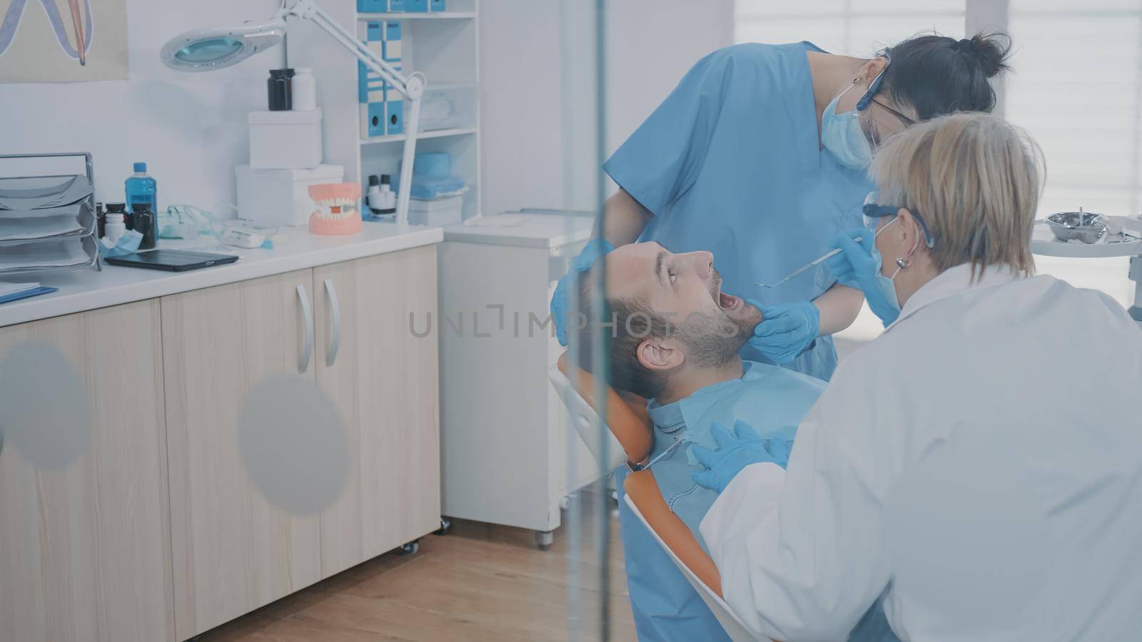 Stomatologist and nurse using dental tools to examine dentition work after surgery at oral care clinic. Dentistry team doing teeth consultation on patient to cure cavity problem.