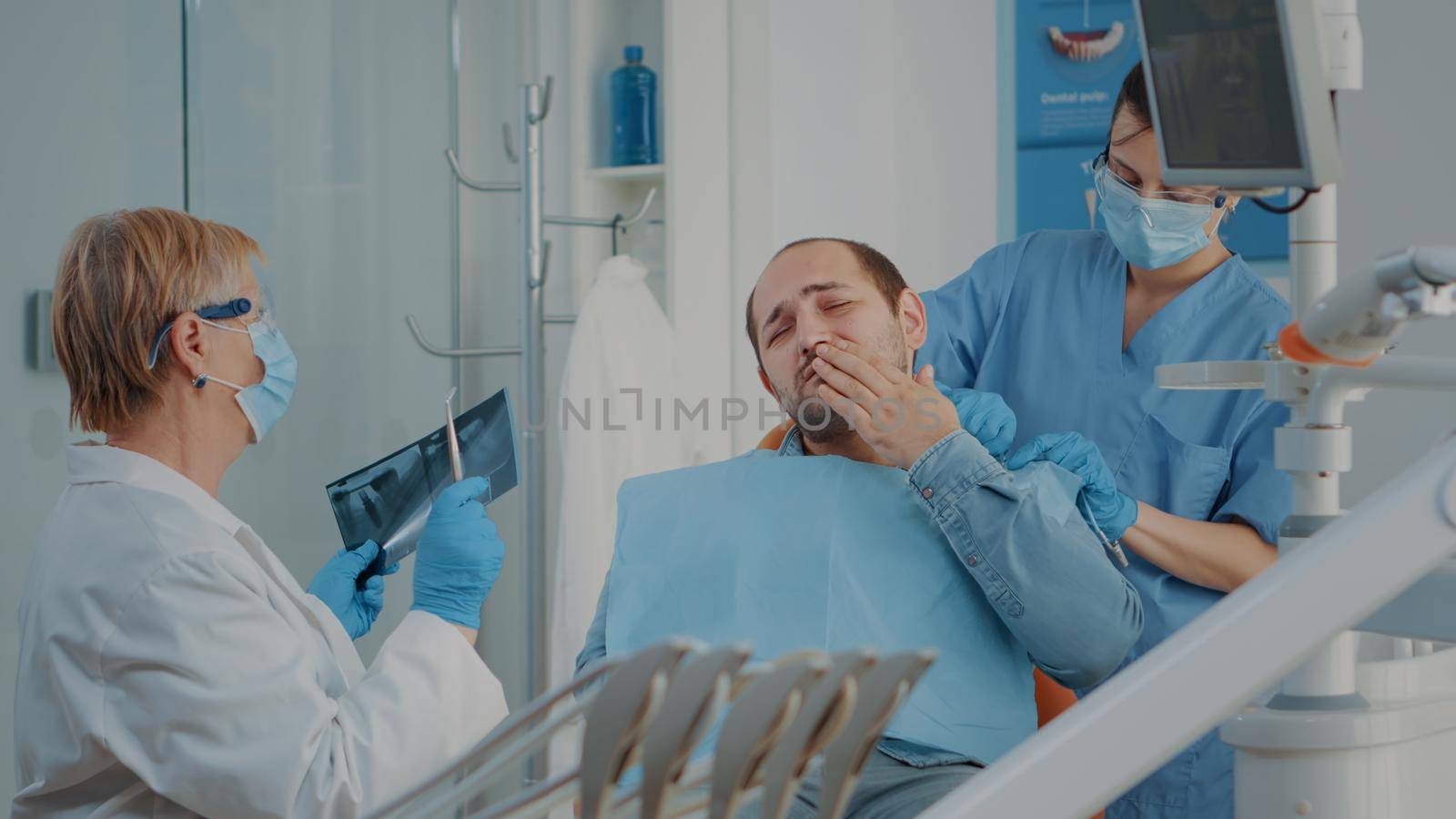 Patient complaining about toothache at stomatology consultation while dentist analyzes dental radiography to do drill procedure. Senior stomatologist treating caries for oral care.