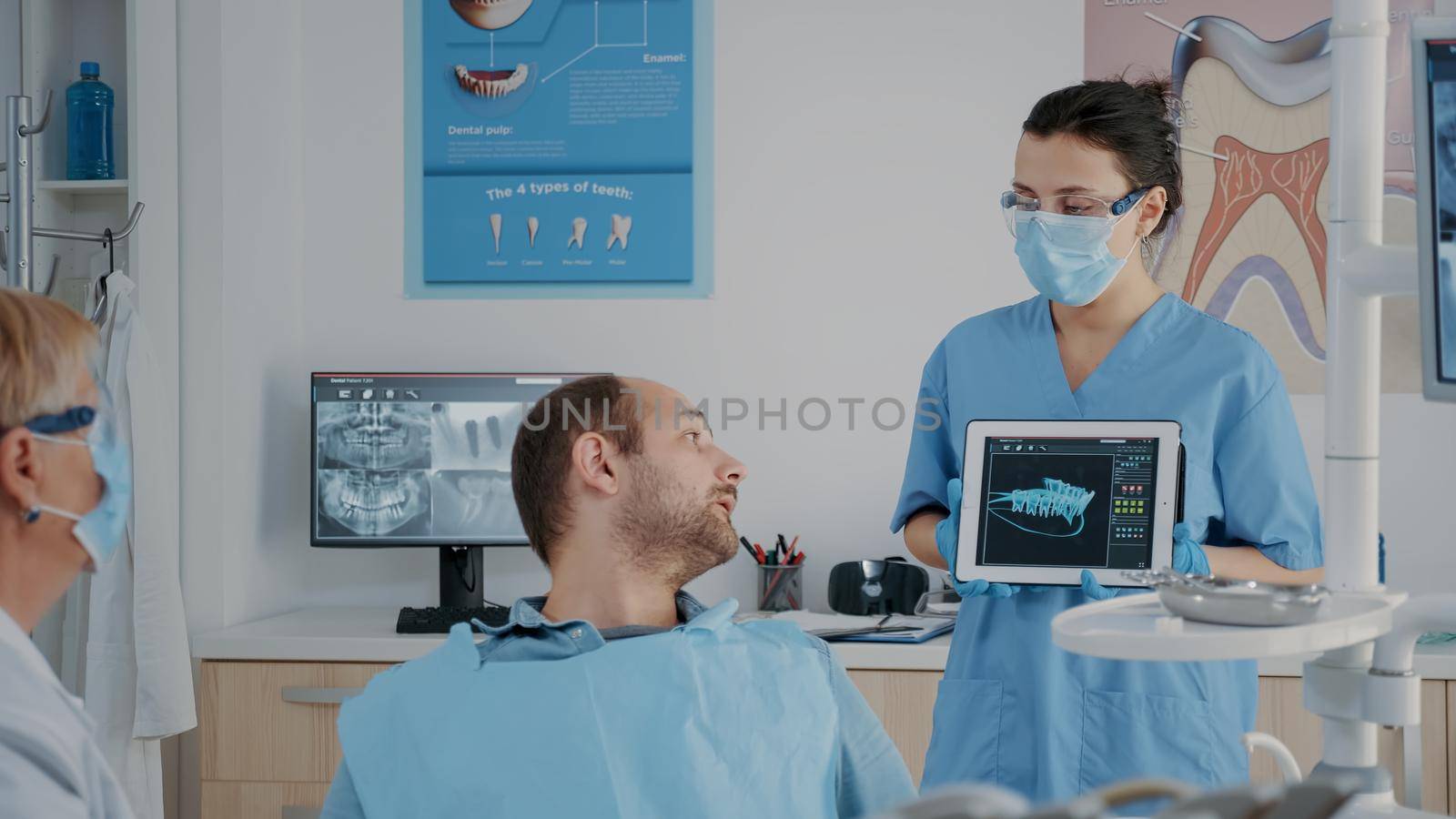 Stomatological team pointing at denture radiography on tablet, showing diagnosis to patient with cavity pain. Nurse and medic explaining x ray scan results at oral care consultation.