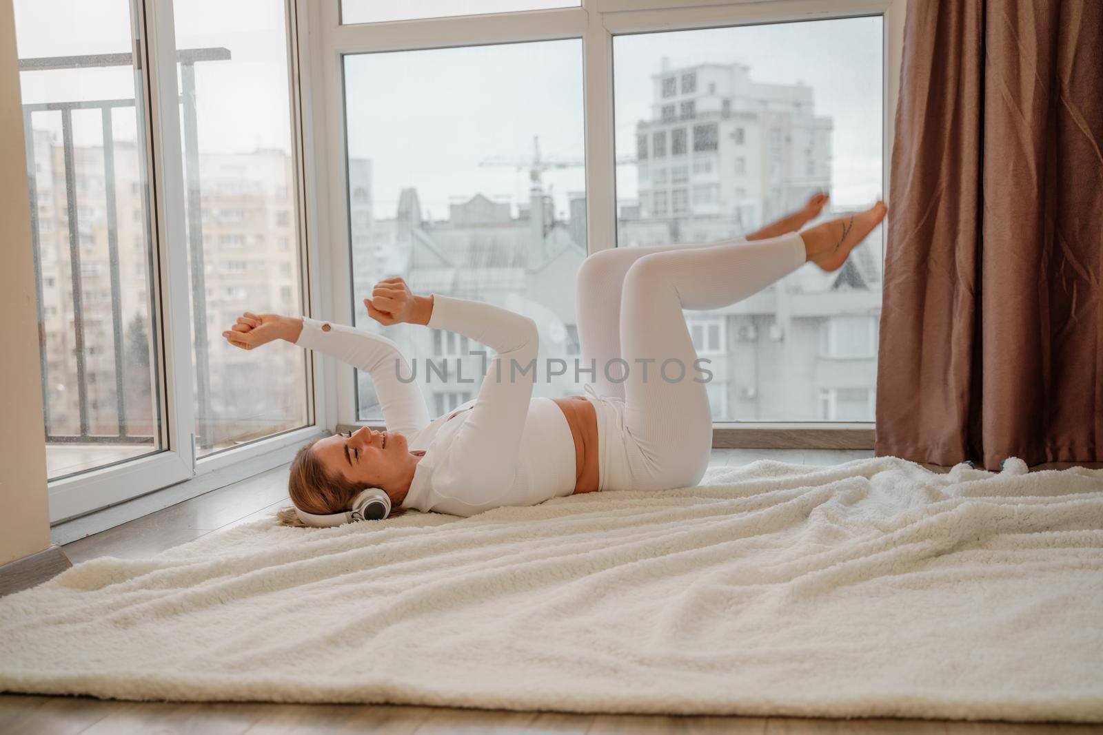 Side view portrait of relaxed woman listening to music with headphones lying on carpet at home. She is dressed in a white tracksuit