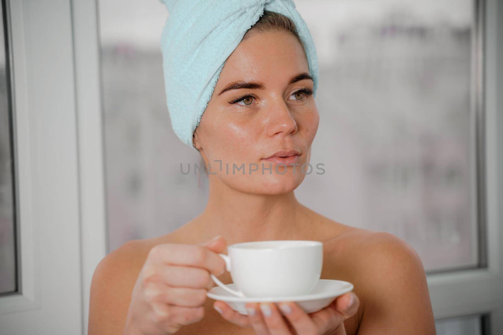 Young serene relaxed woman in spa bath towel drinking hot beverage tea coffee after taking shower bath at home. Beauty treatment, hydration concept