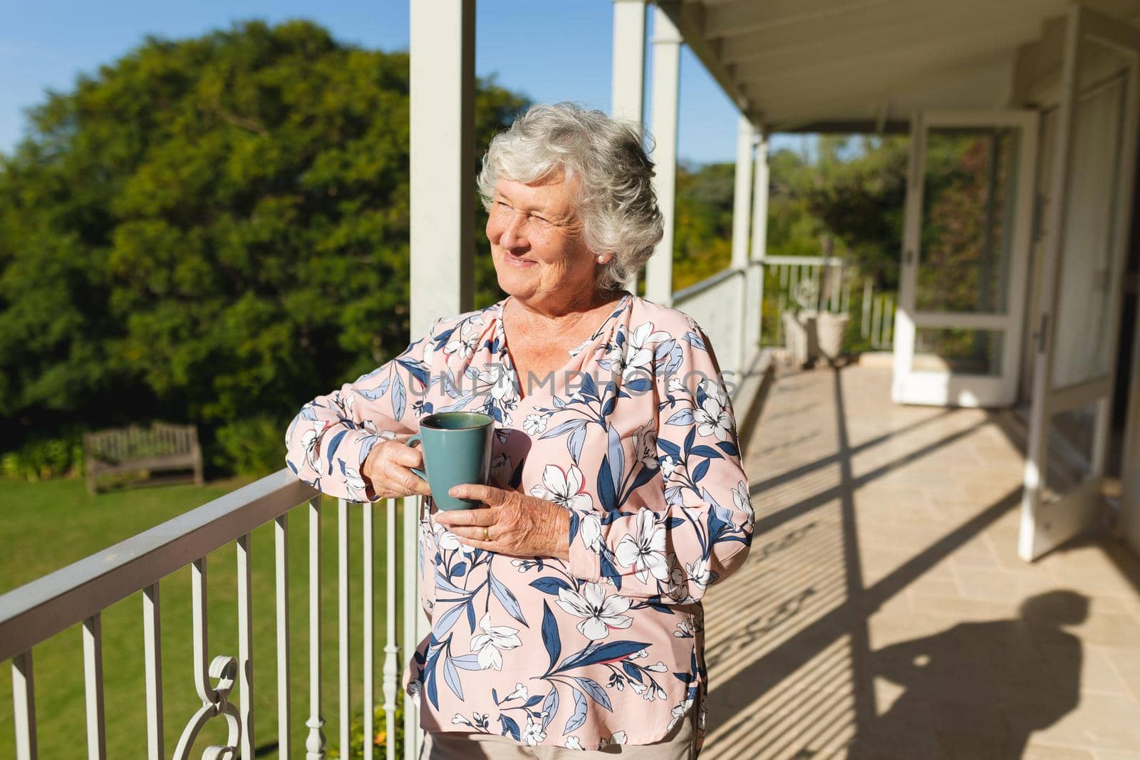 Senior caucasian woman standing on balcony holding mug and smiling. retreat, retirement and happy senior lifestyle concept.