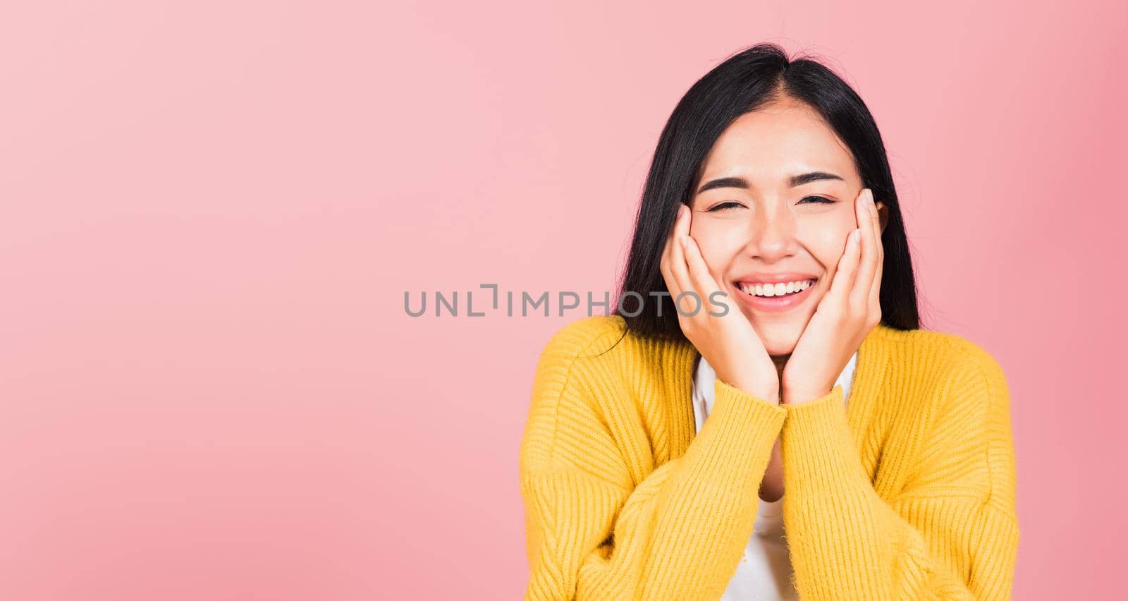 Happy Asian portrait beautiful cute young woman smile holding her cheeks looking to camera studio shot isolated on pink background Thai female beauty face touch massage healthy skin with copy space