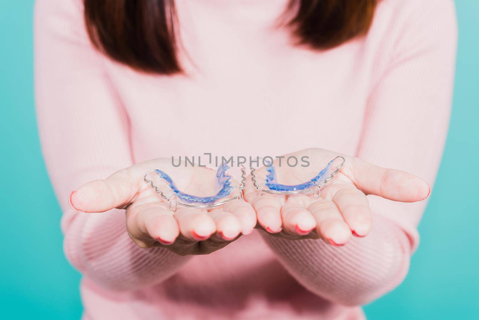 Close up hands of young woman holding silicone orthodontic retainers for teeth, Teeth retaining tools after removable braces, isolated blue background, Dental hygiene healthy care concept